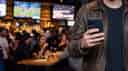 Person at a sports bar with mobile phone in his hand placing bets. 