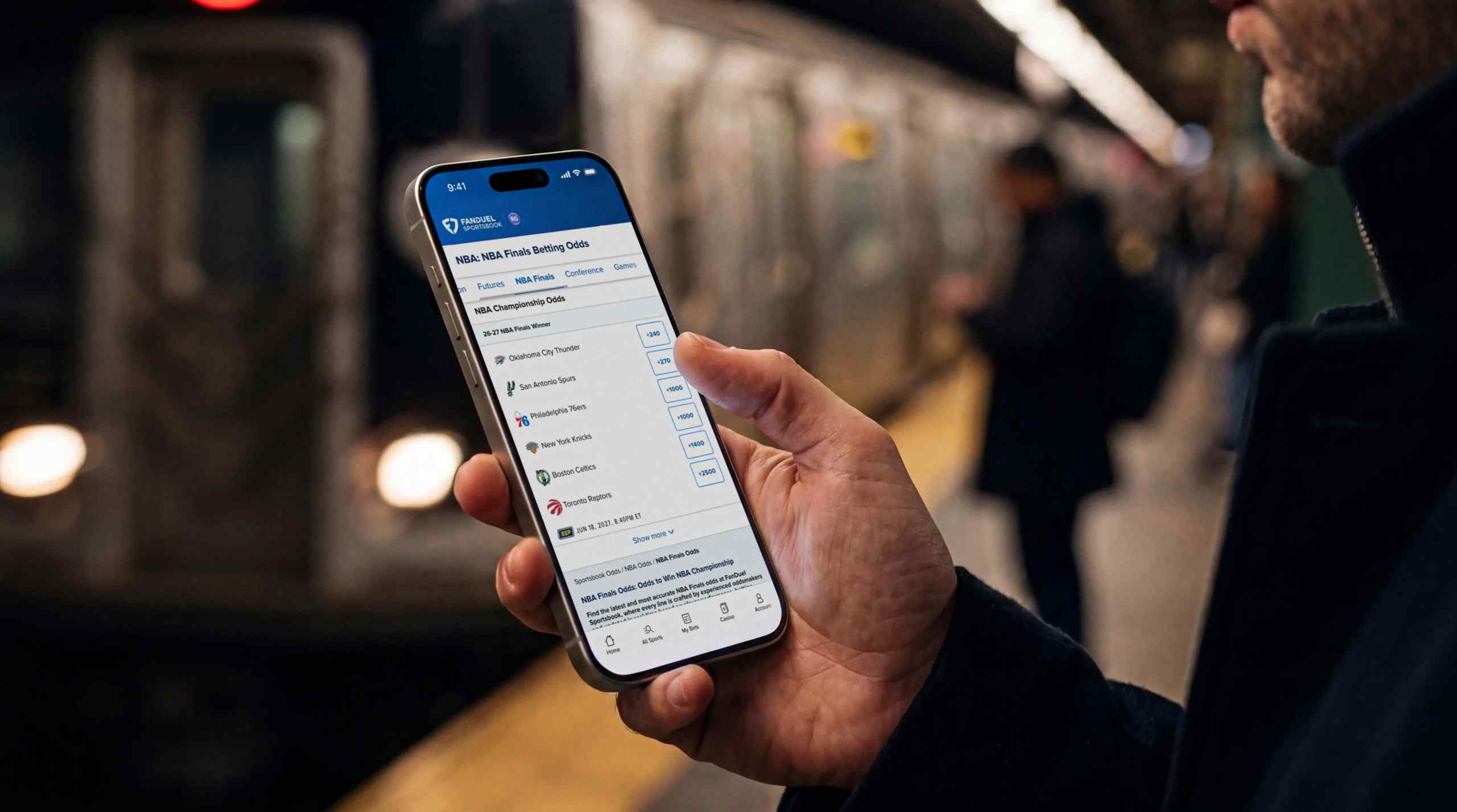 A man checking NBA odds on his mobile phone while waiting for the train.
