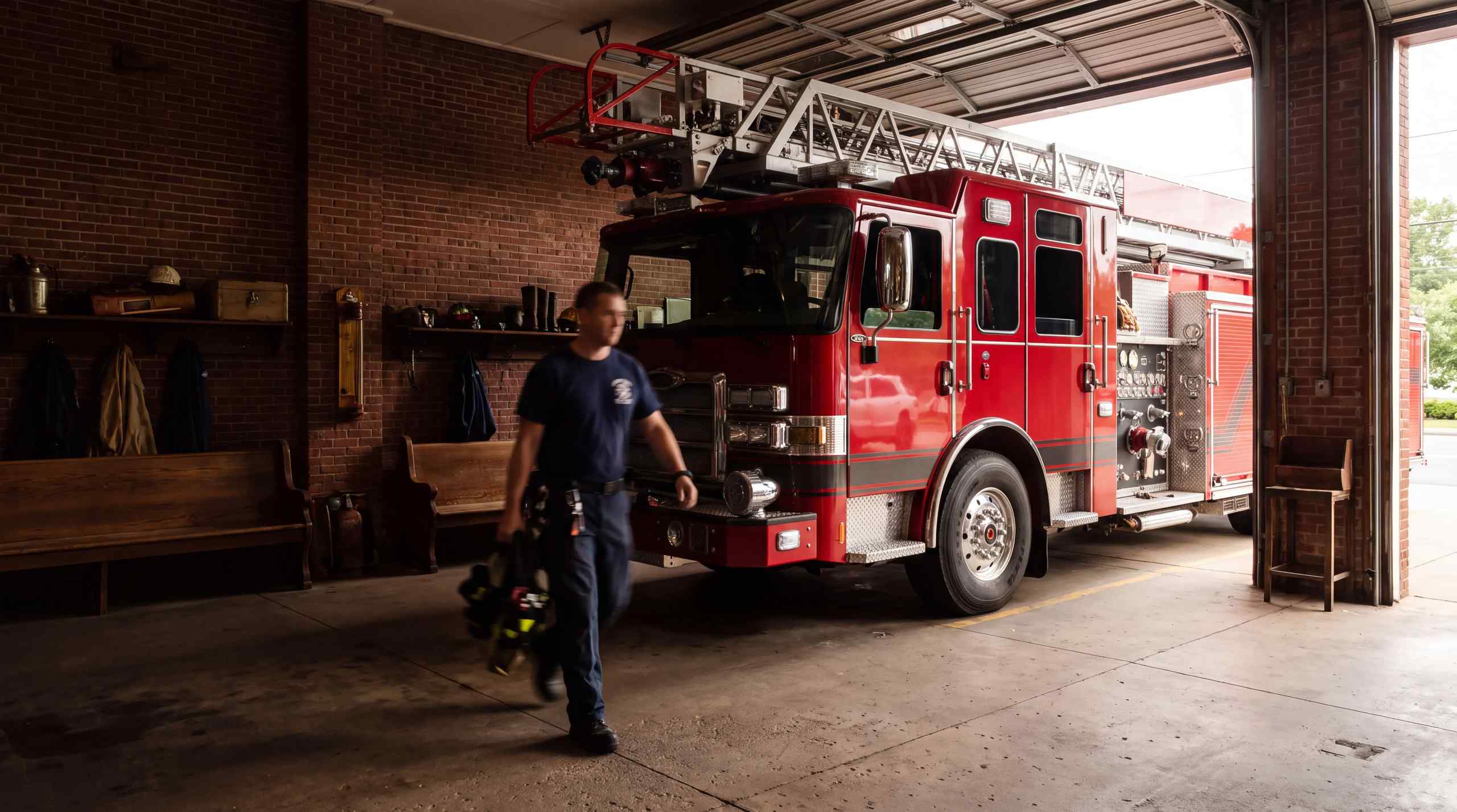 A firefighter walks through the station with a firetruck in the background.