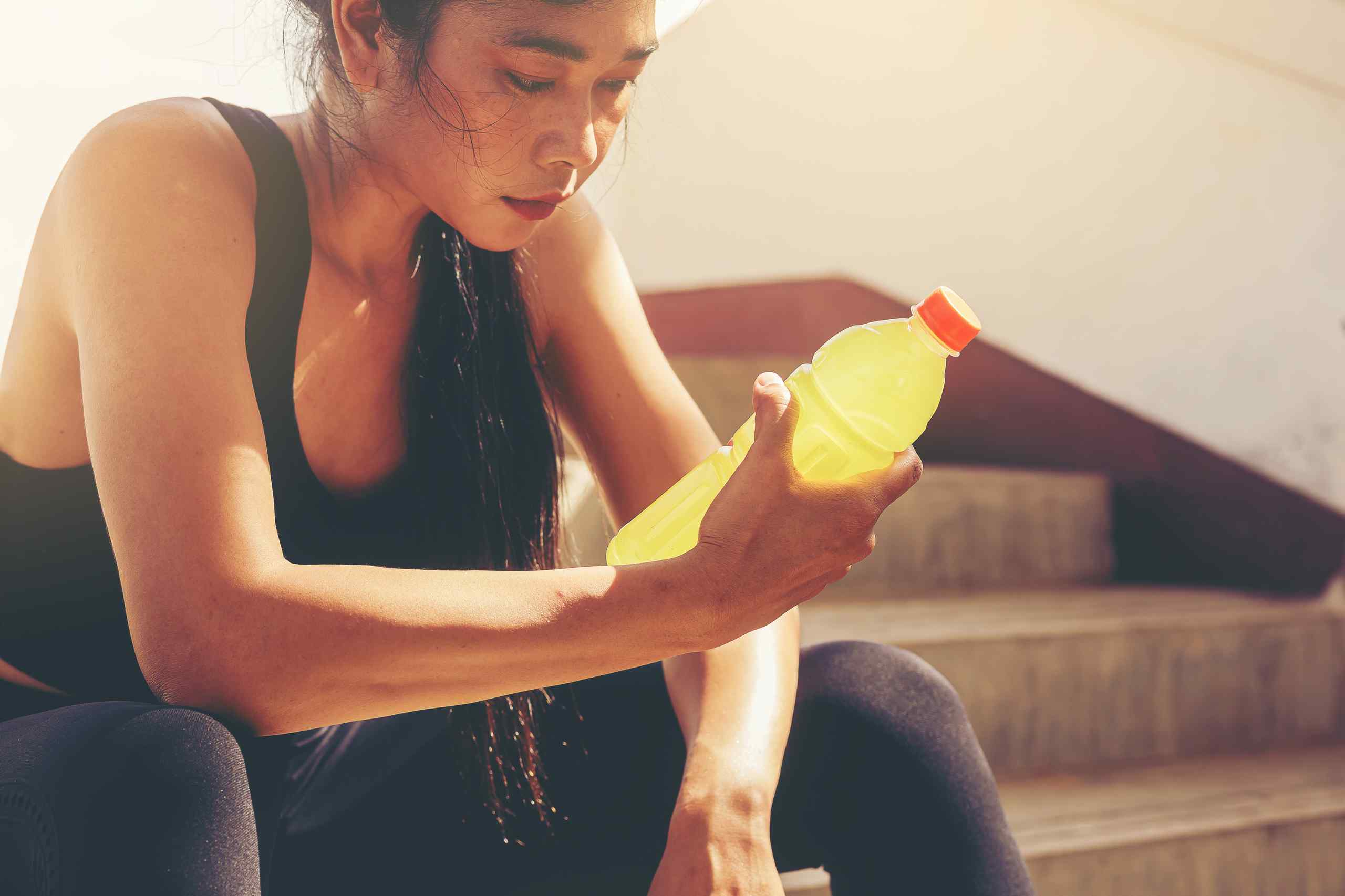 A woman looking down at a sports drink.