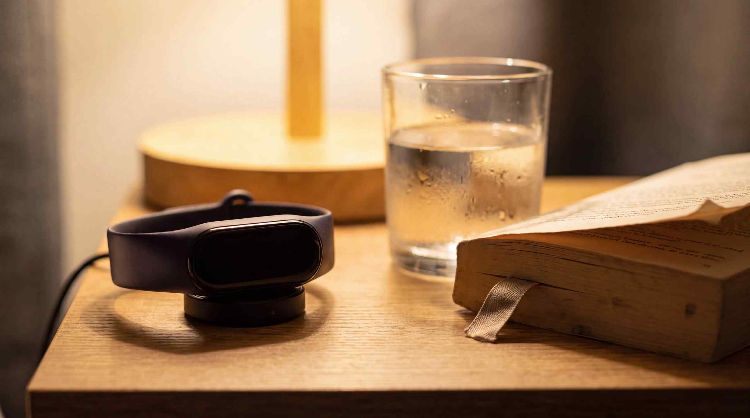 A bedside table featuring a fitness tracker, glass of water and book.