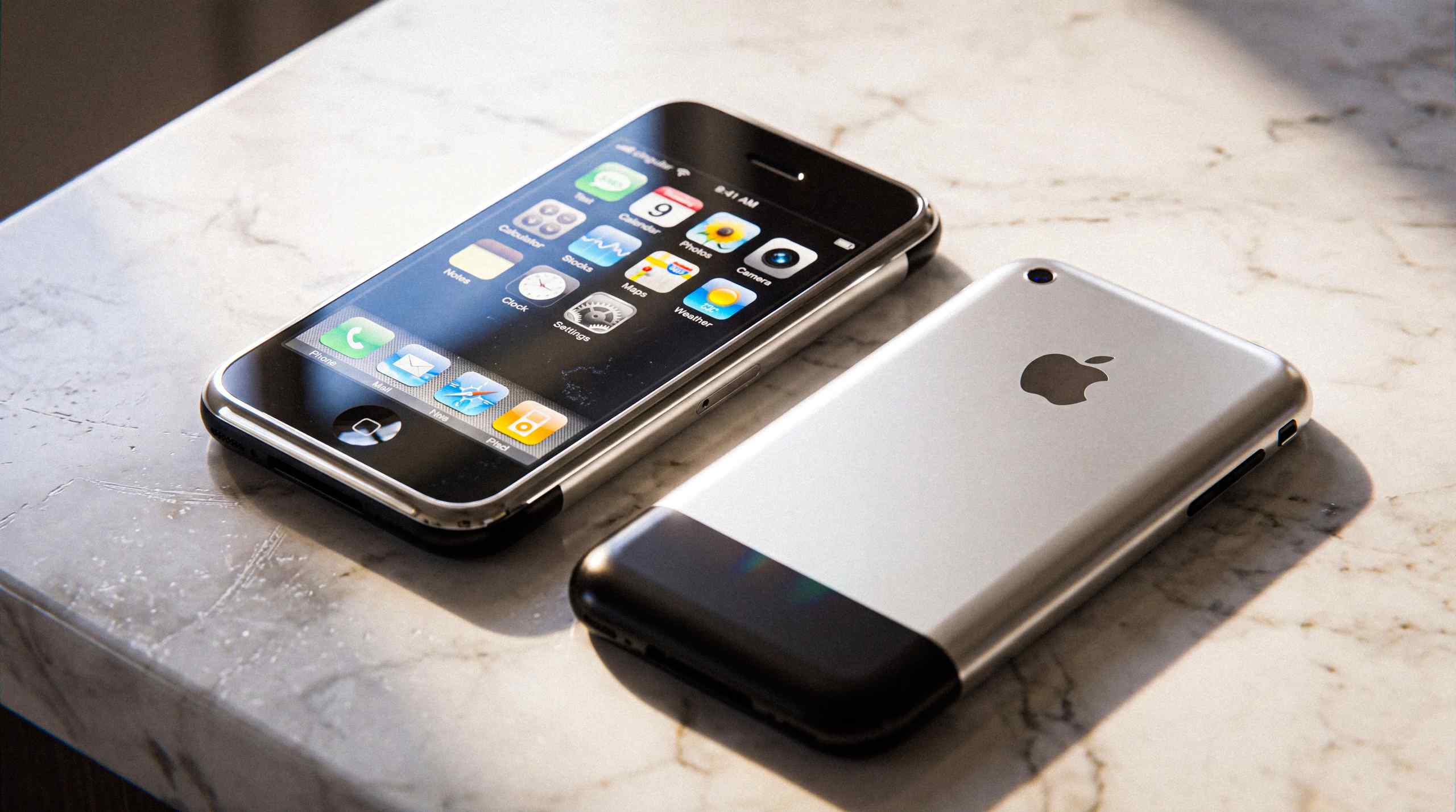 Two original iPhones set on a countertop. One is face up and the other is facedown.