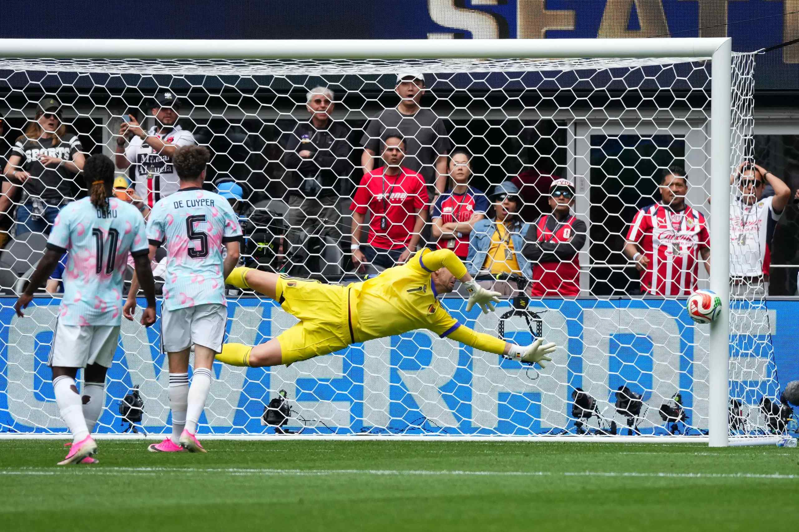 A soccer ball hitting the post with a goalkeeper in full stretch.