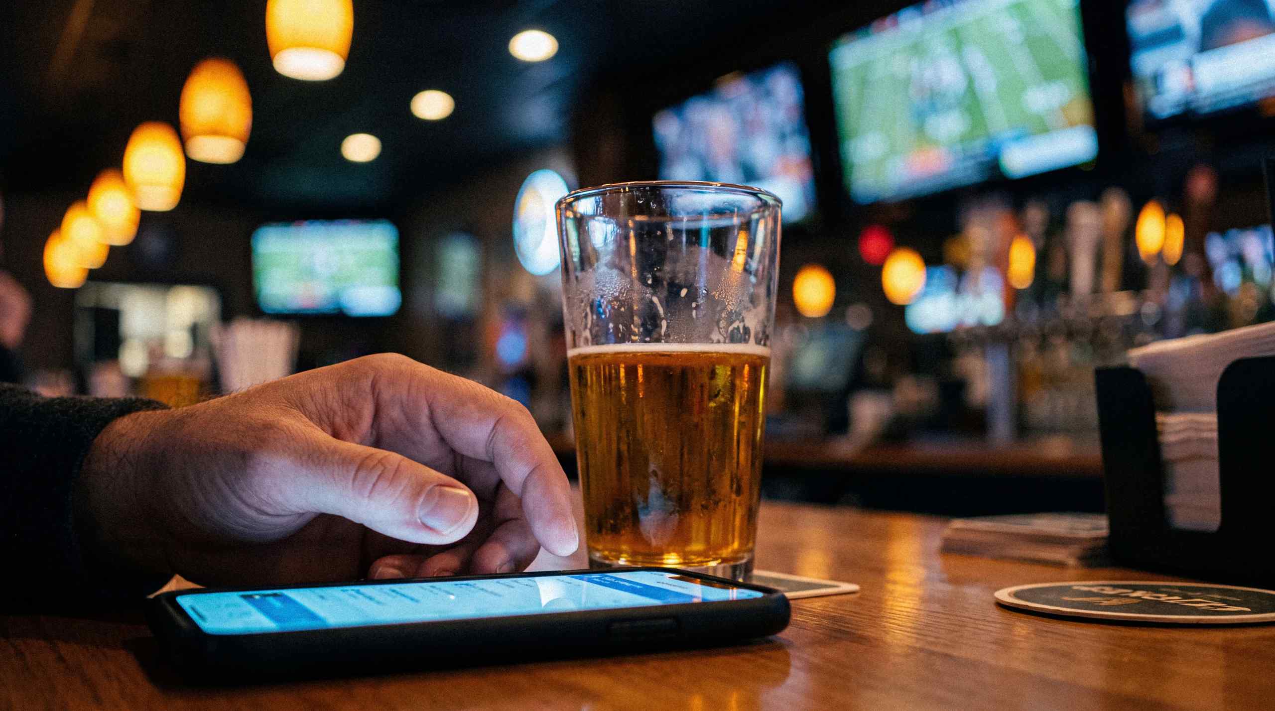 A man checking odds on his phone while enjoying a beer at a bar.