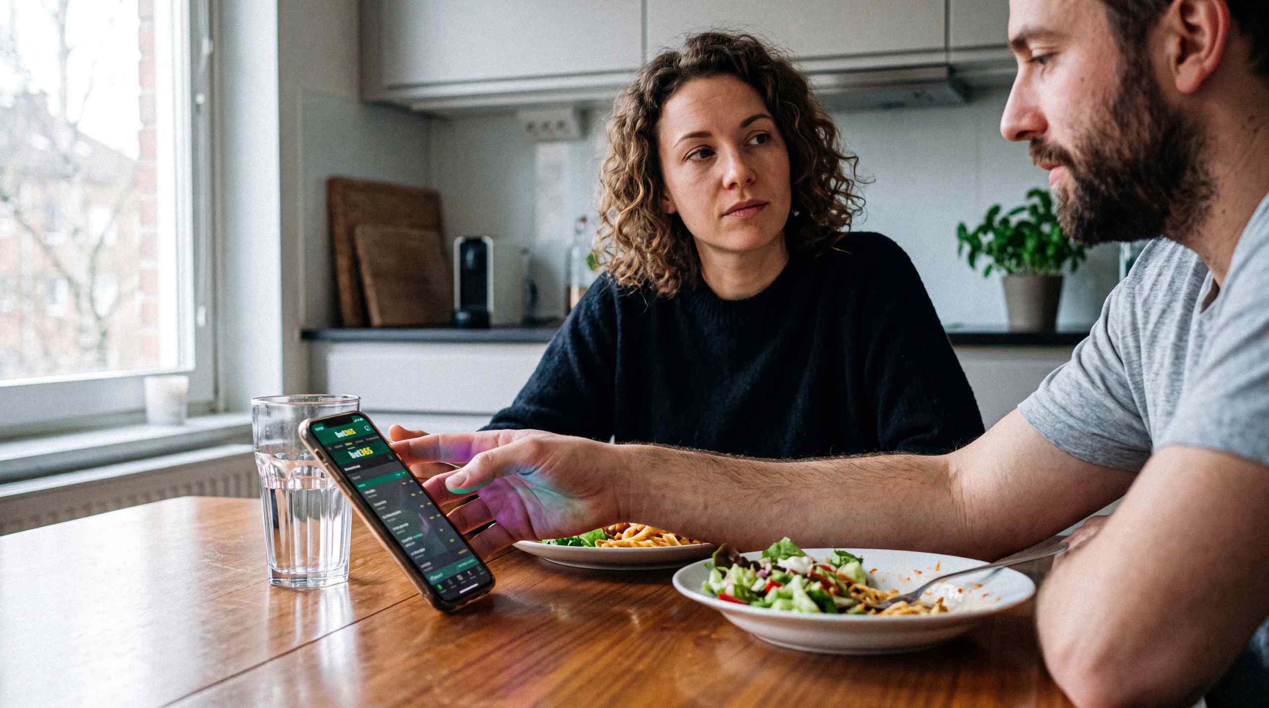 A man looking at his mobile gambling app while a women looks disappointed.