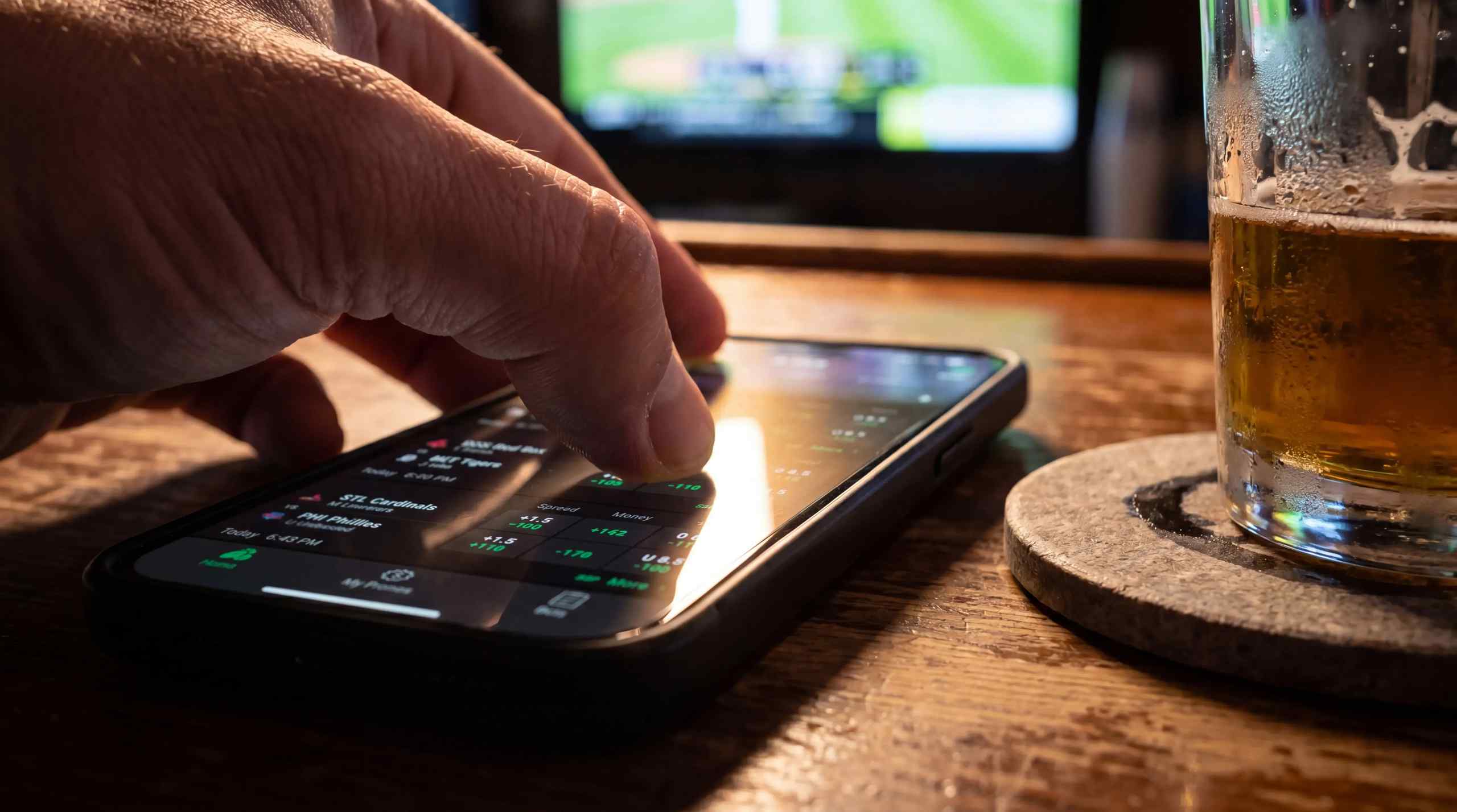a hand scrolling through betting app while watching sports