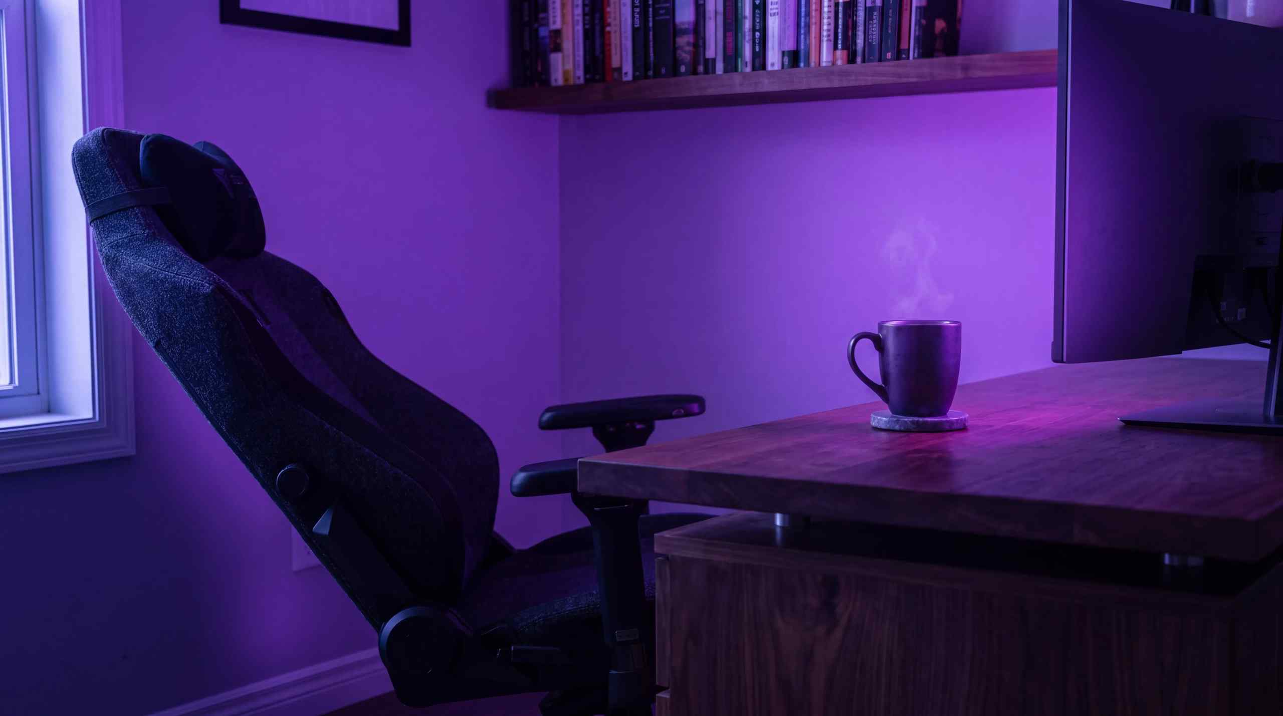 An empty desk chair with a steaming cup of coffee on a desk at night.