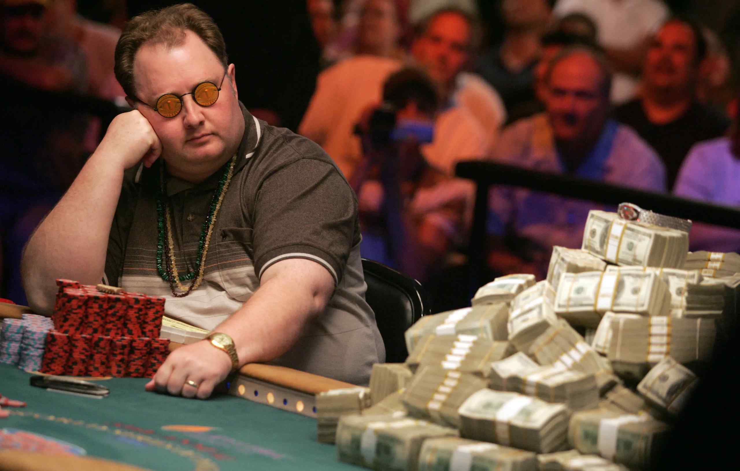 WSOP champ Greg Raymer at a poker table next to a huge stack of cash.